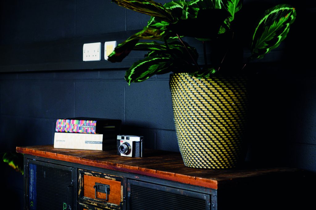 A reclaimed cabinet which is in our team meeting room, with paper sample books, an old camera and a funky plant sat on top