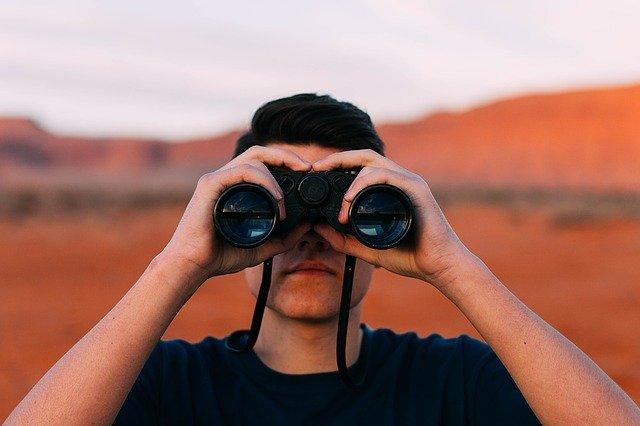 Man looking through binoculars in a desert.