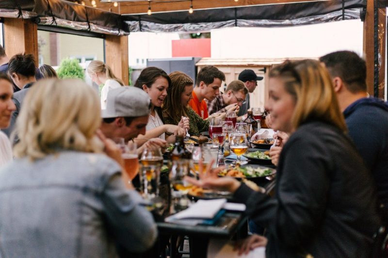 Group of people sat around a large table eating, drinking and talking.