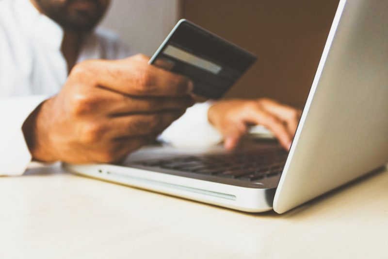 Man holding credit card in front of a white laptop.